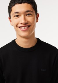 Maglione nero lavorato a maglia con collo a giro, caratterizzato da un logo nero discreto sul petto. Tessuto morbido, di peso medio.