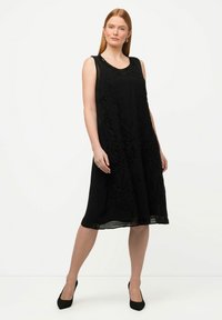 Vestido negro sin mangas con bordado floral, escote redondo y una silueta A-line fluida, que presenta un panel inferior transparente y un forro sólido.