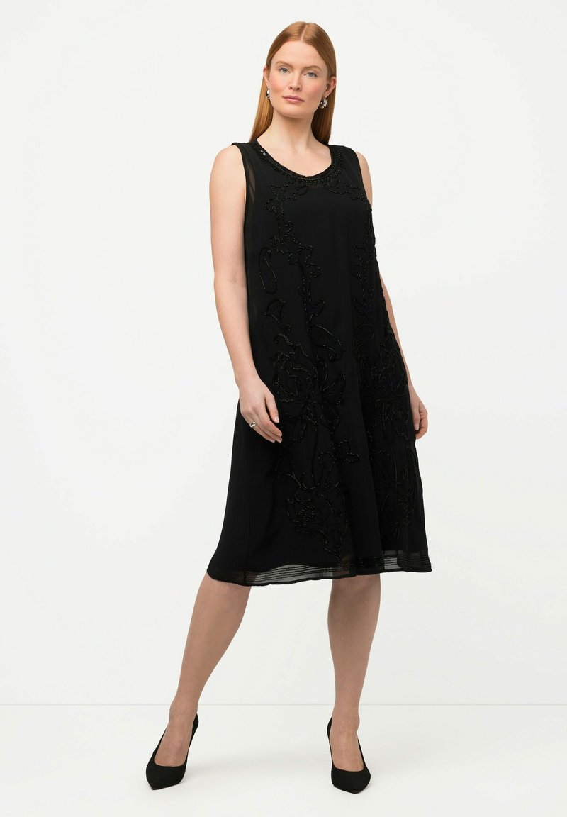 Vestido negro sin mangas con bordado floral, escote redondo y una silueta A-line fluida, que presenta un panel inferior transparente y un forro sólido.