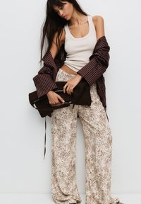Débardeur beige, chemise oversize rayée marron, et pantalon ample crème avec imprime animal marron. Pochette noire texturée tenue devant.