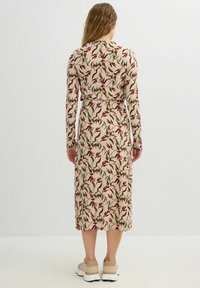 Vestido con estampado floral en beige, con mangas largas, cintura ajustada y largo midi. Combinado con zapatillas de color claro.