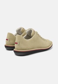 Scarpe in suede beige con profilo basso, sottile bordo rosso e suola nera. Presentano sei fori per i lacci e una morbida fodera interna liscia.