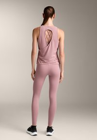 Light pink athletic tank top with a twisted back design, paired with matching leggings. The outfit features a soft, smooth texture and a fitted silhouette.