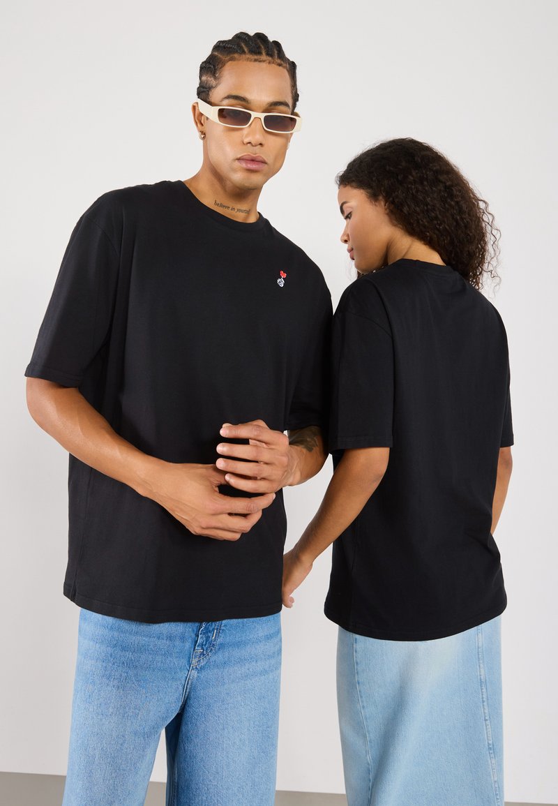 Svart bomulls oversized T-skjorte med et lite rødt og hvitt broderi. Rund hals, korte ermer og en avslappet passform.