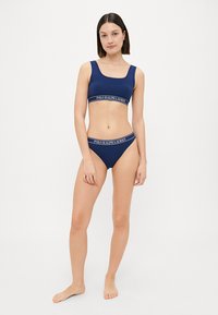 Jūros mėlynos sportinės liemenėlės ir maudymosi kostiumėlio rinkinys su plačiu diržu, ant kurio užrašyta "POLO RALPH LAUREN". Pagamintas iš lygaus, elastingo audinio.