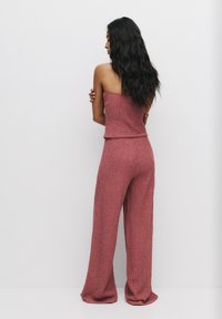 Růžový texturovaný dvoudílný outfit obsahující top bez ramínek a volně padnoucí široké kalhoty. Materiál vypadá měkký a tkaný.