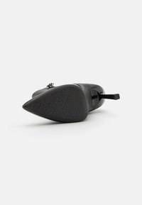 Svart stiletthæl med spiss tå og teksturert såle, med blokk hæl og en blank detalj bak.