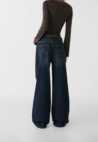 Jeans s širokými nohavicemi v tmavě modré barvě s vybledlým povrchem, s mírně zvýšeným pasem, dvěma zadními kapsami a kontrastním prošíváním.