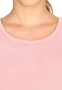 Silverfärgad halskedja med ett renhänge som har intrikata horn och en röd näsa, bärs över en rosa tygtröja.