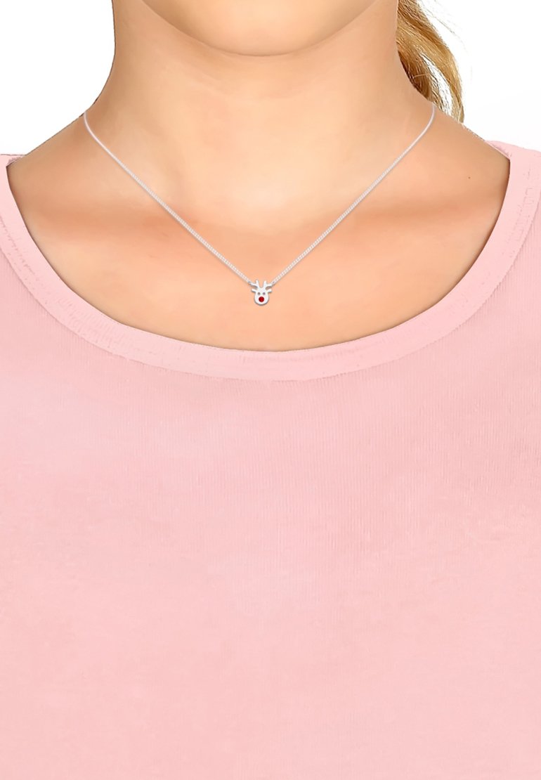 Silverfärgad halskedja med ett renhänge som har intrikata horn och en röd näsa, bärs över en rosa tygtröja.