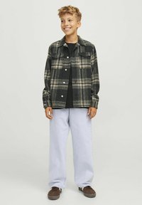 Camisa de franela a cuadros en negro y beige, con dos bolsillos en el pecho y cierre de botones. Combinada con pantalones holgados de color azul claro y zapatos marrones.