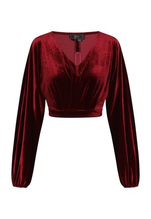 Červený sametový crop top s dlouhými, objemnými rukávy a hlubokým véčkovým výstřihem. Disponuje sklady a uzávěrem na zádech s střapcem.