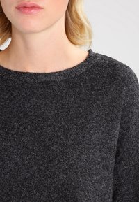 Ciemnoszary sweter o okrągłym dekolcie, dzianinowej fakturze i miękkim materiale. Posiada prosty design bez ozdobników czy wzorów.