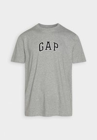 Camiseta de algodón gris con cuello redondo, mangas cortas y logo bordado en negro "GAP" encima del pecho. Textura suave, diseño casual.