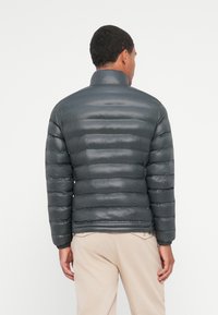 Giacca a vento grigia scura con una trama liscia, cuciture orizzontali e colletto alto. I polsini e l'orlo sono elasticizzati per una vestibilità perfetta.