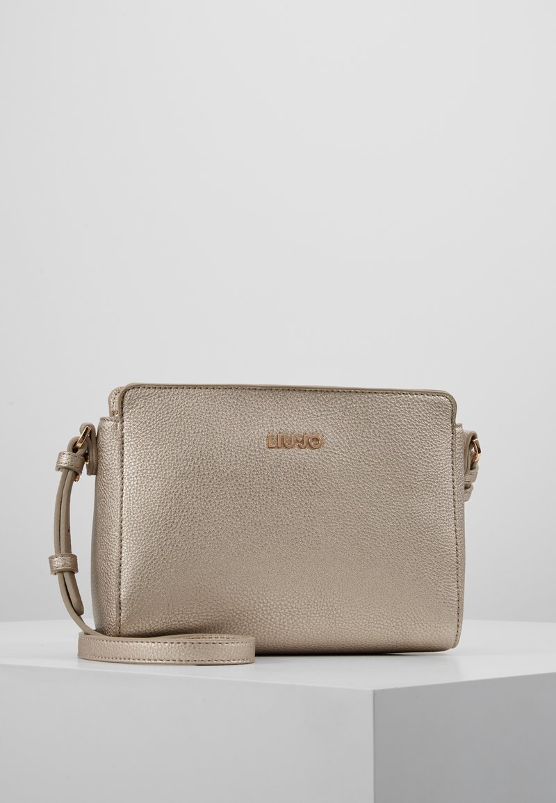 Bolso bandolera metálico en color dorado con superficie texturizada, correa ajustable, cierre con cremallera y logotipo grabado en la parte frontal. Diseño compacto y rectangular.
