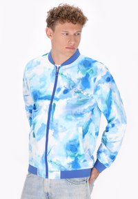 Blauwe bomberjack met abstract aquarelontwerp in tinten blauw en groen, met een rits, geribbelde manchetten en twee zijzakken.