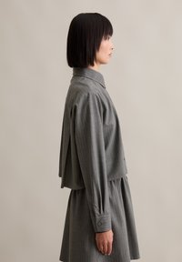 Siva jakna s prugicama, skraćena, s visokim ovratnikom, slojevitim materijalom i dugim rukavima, u kombinaciji s odgovarajućom suknjom, bočni prikaz.