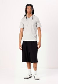 Gråstribet kortærmet T-shirt med V-hals, parret med sorte shorts i knæ-længde. Modellen har grå og sorte sportssko på samt hvide sokker.
