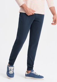 Marineblauwe joggingbroek met een slim fit, voorzien van zijzakken en geribbelde boorden, gecombineerd met blauwe sportieve schoenen.