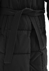 Abrigo acolchado negro con textura de acolchado y un cinturón a juego. El cinturón tiene un diseño de rayas verticales y se ata en la cintura para un ajuste ceñido.