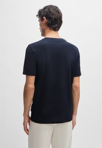 Marineblå t-shirt med korte ærmer, rund hals, struktureret stof og afslappet pasform, der har et diskret logo tag i kanten.