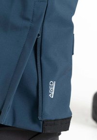 Wasserdichte Jacke aus dunkelblauem Stoff mit einer Reißverschlusstasche, schwarzen Akzenten und einem weißen Logosticker an der Seite. Schlankes, eng anliegendes Design.