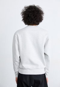 Grey sweatshirt with long sleeves, crew neck, and ribbed cuffs. Fabric appears soft with a smooth texture, featuring a relaxed fit.