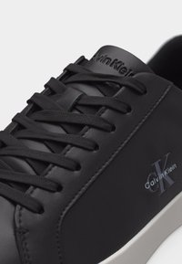 Μαύρο δερμάτινο αθλητικό παπούτσι Calvin Klein με μαύρα κορδόνια και λευκή σόλα, με ανάγλυφο λογότυπο "CK" και "Calvin Klein" στην πλευρά.