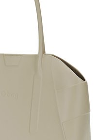 Beige Tragetasche aus weichem, flexiblem Material. Verfügt über ein minimalistisches Design mit glatter Textur und zwei langen Tragegriffen.