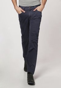 Bawełniane spodnie w kolorze granatowym z prostą nogawką, z przednimi kieszeniami i subtelnymi detalami szwów. Noszone z szarą bluzką i czarnymi butami.