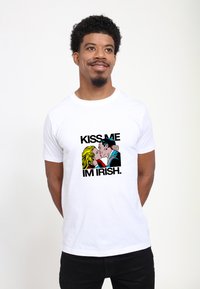 Bílý bavlněný tričko s grafikou páru, který se líbá, a textem "KISSE ME I'M IRISH." v tučných černých písmenech.