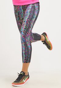 Leggings noirs avec un motif ondulé vibrant en rose, bleu et vert ; associés à des chaussures de course noires et néon.