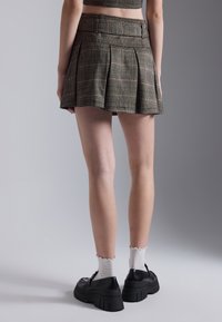 Plaid mini skirt in brown tones with pleats, featuring a high waist and subtle stitching details. Worn with black platform shoes and white socks.