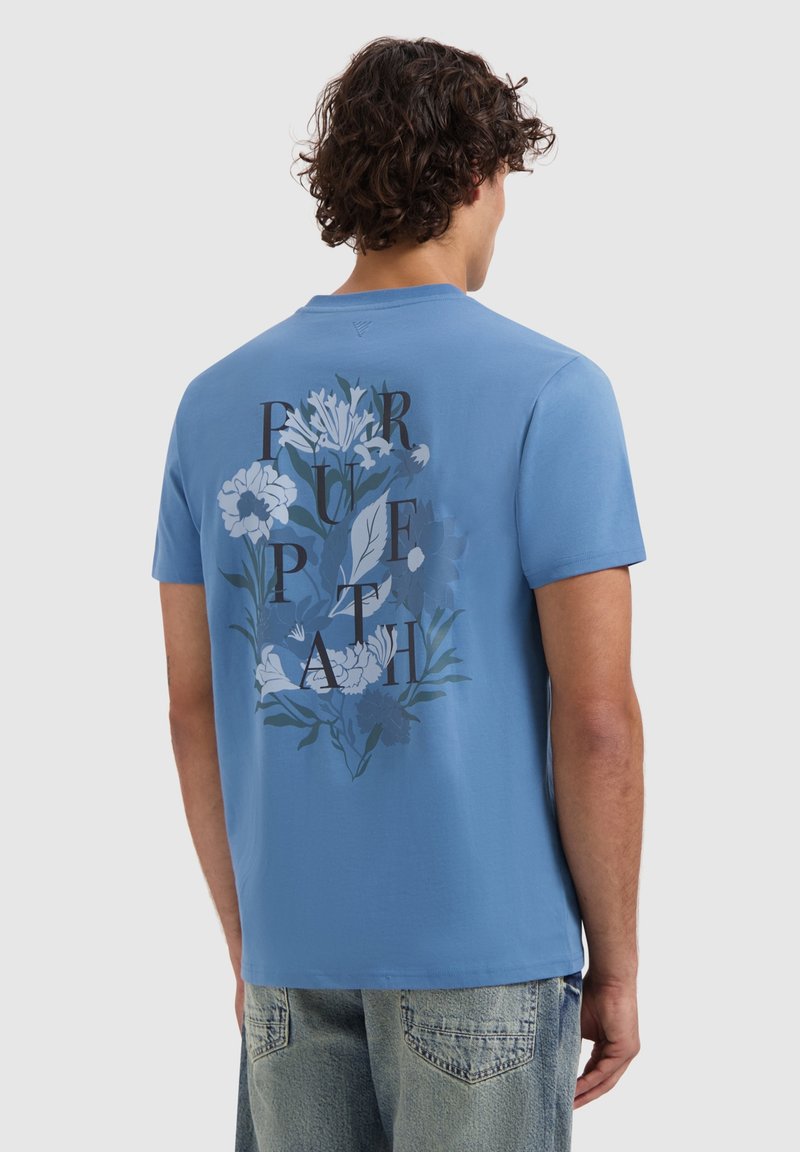 Blauwe katoenen t-shirt met een bloemmotief op de achterkant en de tekst "PURPLE PATH" in vette zwarte letters. Korte mouwen, ronde hals.