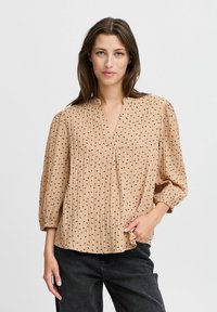 Beige Bluse mit vertikalen Streifen und kleinen schwarzen Herzmustern, mit lässiger Passform, V-Ausschnitt und langen Ärmeln mit elastischen Bündchen.