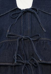 Donkerblauwe denim kleding met een v-hals ontwerp, voorzien van een vastgebonden trekkoord in de taille en een gerimpelde textuur langs de zoom.
