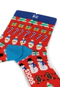 Chaussettes rouges avec des motifs festifs, comprenant des bonhommes de neige, des cannes en sucre, des arbres et des cadeaux. Accents bleus sur le talon et sur le poignet côtelé.