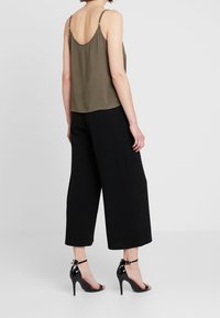 Haut sans manches vert olive avec un dos décolleté, associé à un pantalon noir large et des sandales à talons noires, avec des brides aux chevilles.