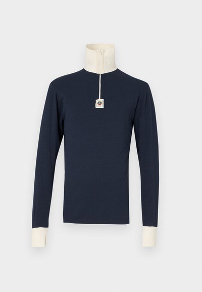 Navy long-sleeve polo shirt with a high neck, ivory collar, and cuffs. Features a small logo patch on the front. Soft material, slim fit.