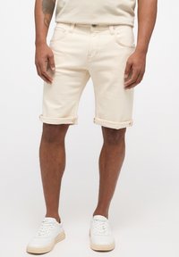 Shorts en denim beige avec ourlets retroussés, dotés de poches avant et d'un design classique à cinq poches, associés à des baskets blanches.