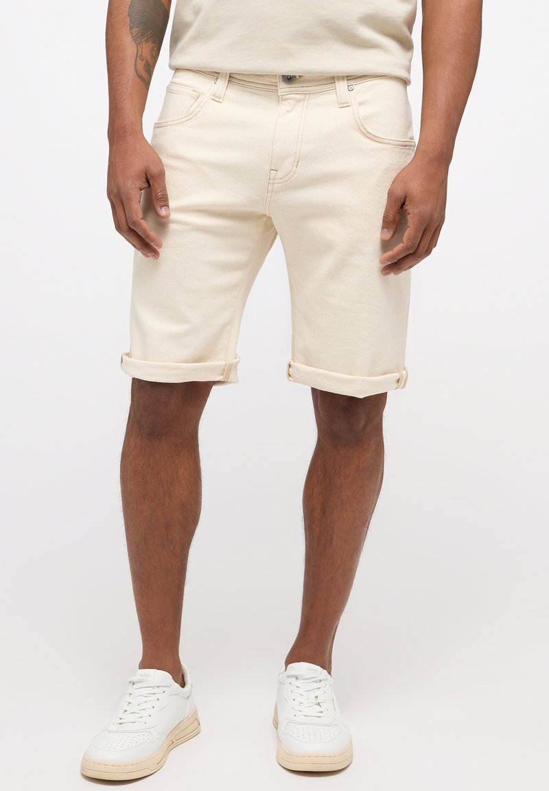 Shorts en denim beige avec ourlets retroussés, dotés de poches avant et d'un design classique à cinq poches, associés à des baskets blanches.