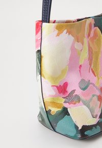 Borsa a tracolla con motivo floreale nei colori rosa, giallo, verde e bianco, con manici blu scuro e rifiniture nere su sfondo bianco.