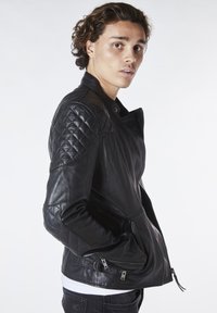 Svart läderjacka med kviltad axeldetalj, asymmetrisk dragkedjestängning och dragkedjefickor. Slät textur med åtsittande design.