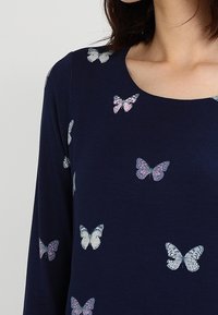 Marinblå långärmad topp med spridda fjärilstryck i vitt och rosa, rund halsringning och mjuk tygkvalitet.