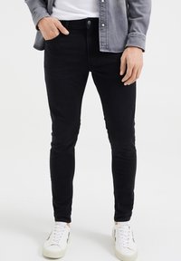 Černé skinny džíny vyrobené z denimu, s klasickým pětipocket designem, zapínáním na knoflík a hladkou texturou. V kombinaci s bílými teniskami.