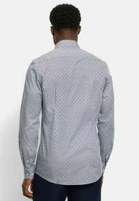 Herren Langarmhemd in Hellblau mit geometrischem Muster in Weiß und Marineblau. Mit Kentkragen und Manschetten mit Knöpfen.