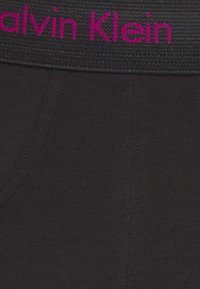 Schwarze Baumwollkleidung mit einem strukturierten Bund, verziert mit rosa "Calvin Klein"-Branding. Der Stoff ist glatt mit dezenten Nahtdetails.