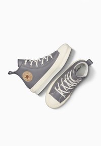 Zapatillas altas de lona gris con un acabado texturizado, suelas de goma blanca y ojales. Presenta un parche de logo circular en el costado.