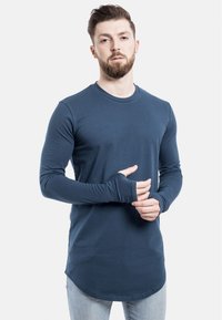 Langærmet navy blå skjorte lavet af blød stof, med rund halsudskæring og tommelfingerhuller i manchetten; buet kantdesign.